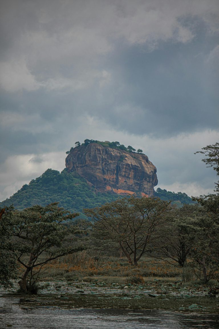 Scenic view of Sigiriya rock fortress amidst lush green nature under cloudy sky in Sri Lanka.
